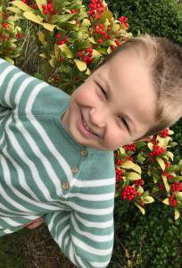 Boy wearing green and white stripe jumper in front of bush