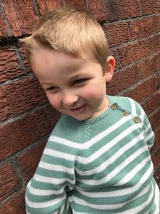 boy wearing green and white stripe jumper in front of wall