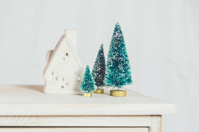 Three miniature Christmas trees next to a white house ornament
